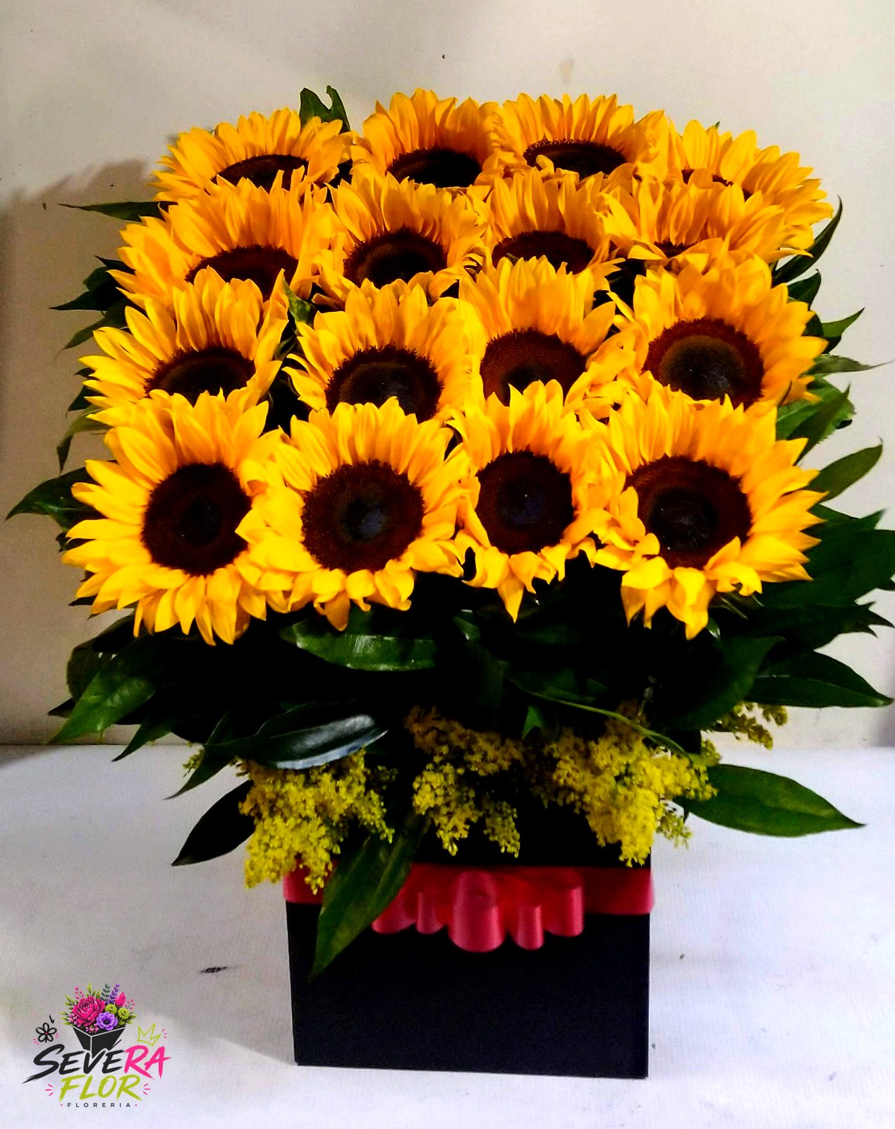 Severo Muro: Bloque compacto de girasoles en base negra. Arreglos Florales Severa Flor Bogotá